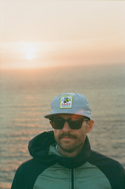 man wearing alki supply eagle eye hat with sunset background